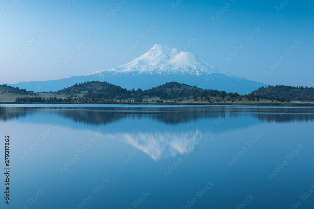 A reflection of snow capped Mount Shasta in a clear water in lake  at sunrise in California State, USA.  Mount Shasta is a volcano at the southern end of the Cascade Range in Siskiyou County 