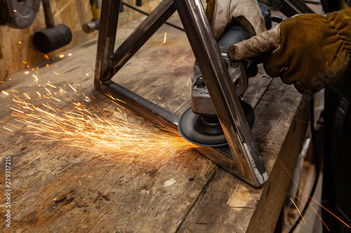 Metalworker uses disc grinder on steel. A closeup view of hot sparks flying from the abrasive disc of an angle grinder whilst a blacksmith polishes a metal frame. photo
