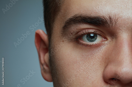 Close-up portrait of young man isolated on grey studio background. Caucasian male model's face and blue eye. Concept of men's health and beauty, self-care, body and skin care, medicine or phycology.