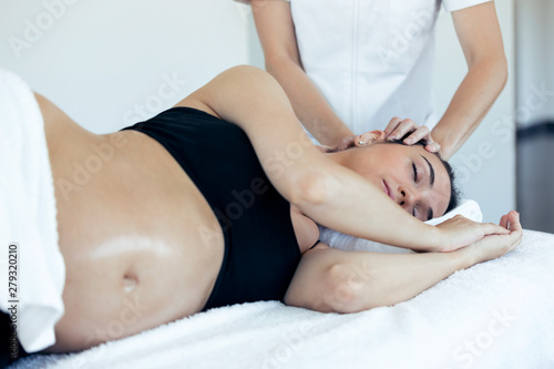 Pregnant woman receiving osteopathic or chiropractic treatment in neck in a clinic.