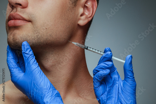 Close-up portrait of young man isolated on grey studio background. Filling botox surgery procedure. Concept of men's health and beauty, cosmetology, self-care, body and skin care. Anti-aging. photo