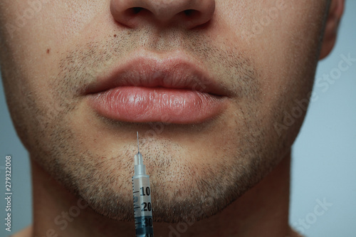 Close-up portrait of young man isolated on grey studio background. Filling botox surgery procedure. Concept of men's health and beauty, cosmetology, self-care, body and skin care. Anti-aging. photo