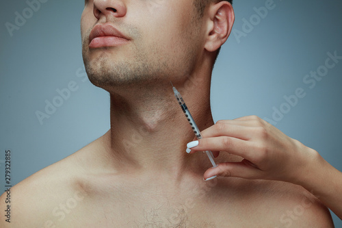 Close-up portrait of young man isolated on grey studio background. Filling botox surgery procedure. Concept of men's health and beauty, cosmetology, self-care, body and skin care. Anti-aging. photo