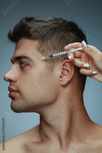 Close-up profile portrait of young man isolated on grey studio background. Filling botox surgery procedure. Concept of men's health and beauty, cosmetology, self-care, body and skin care. Anti-aging. photo