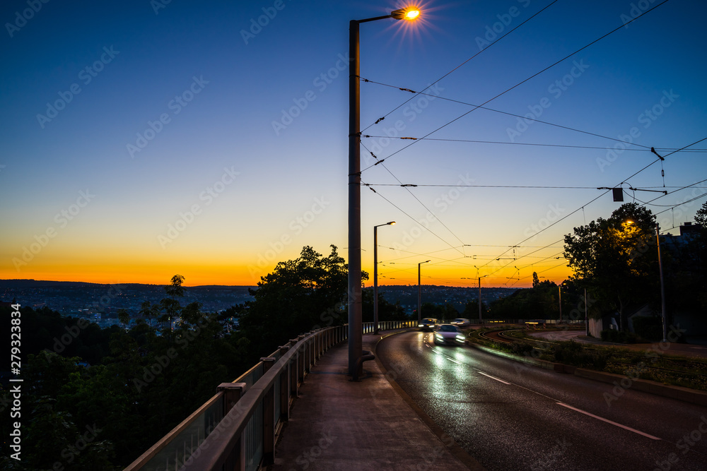 Germany, Cars driving on a road through city stuttgart in magical dawning twilight after sunset near eugensplatz next to rails of tram in summer