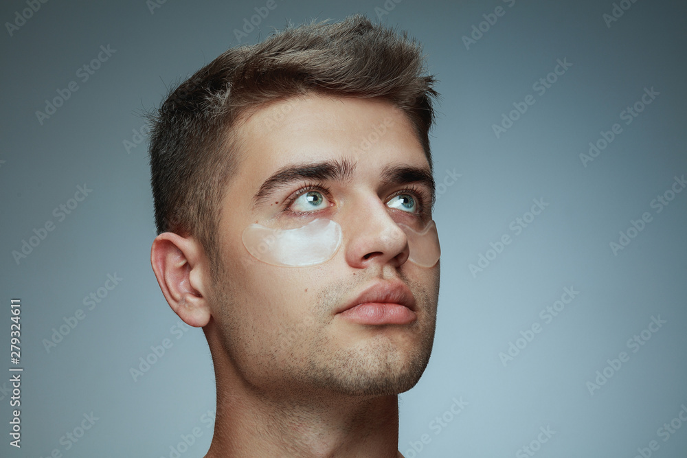 Obraz premium Close-up profile portrait of young man isolated on grey studio background. Male face with collagen patches under eyes. Concept of men's health and beauty, cosmetology, body and skin care. Anti-aging.