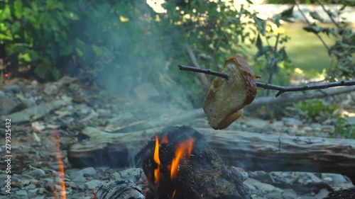 A piece of bread is fried on a stick over a fire in a forest by the river. concept - vacation. photo