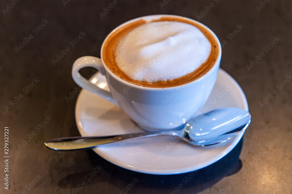 Freshly brewed coffee in coffeehouse. A close-up shot of a just served frothy cappuccino on a table inside a coffee shop, hot morning drink prepared in a white porcelain cup and saucer. Freshly brewed coffee in coffeehouse. A close-up shot of a just served frothy cappuccino on a table inside a coffee shop, hot morning drink prepared in a white porcelain cup and saucer.
