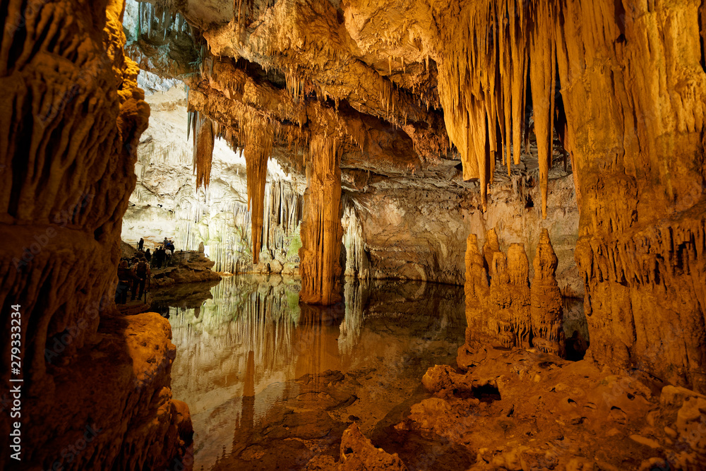 Imposing stalactites and stalacmites reflecting in a small underground lake inside the limestone cave (Tropfsteinhöhle) Grotta di Nettuno in Sardegna (Italy)