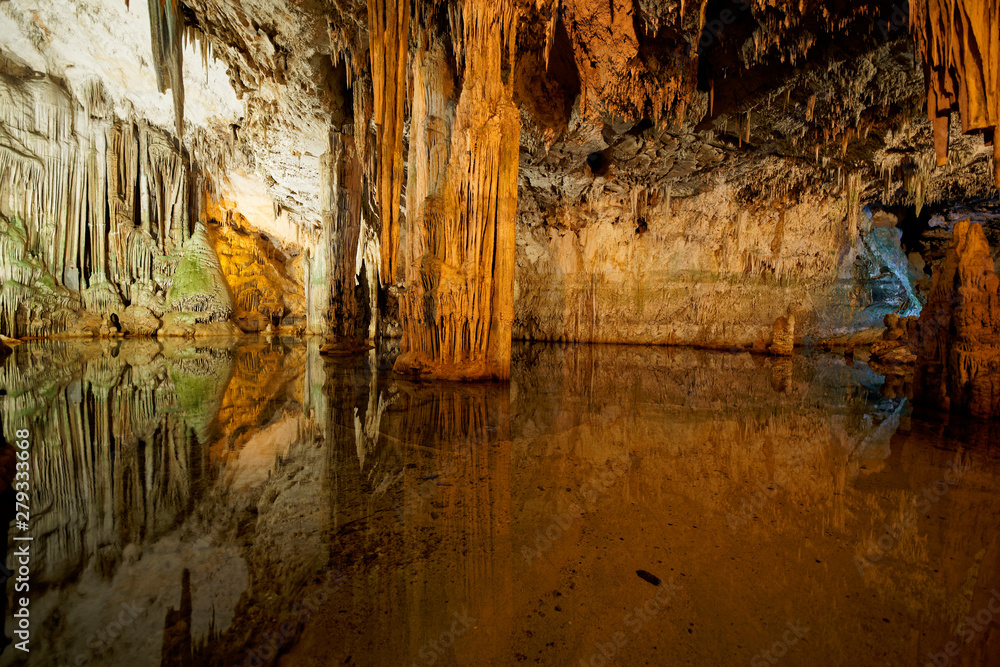 Imposing stalactites and stalacmites reflecting in a small underground lake inside the limestone cave (Tropfsteinhöhle) Grotta di Nettuno in Sardegna (Italy)