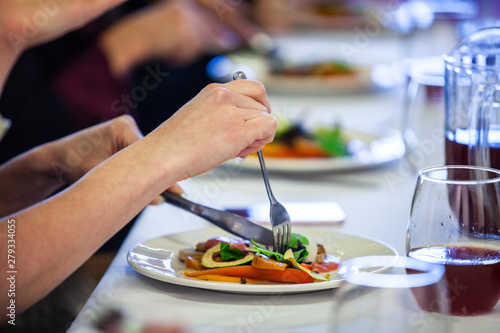 Food served at a conference lunch break. A close up and side view of a woman's hands using a knife and fork to eat a freshly prepared avocado salad during a conference lunch in formal setting.