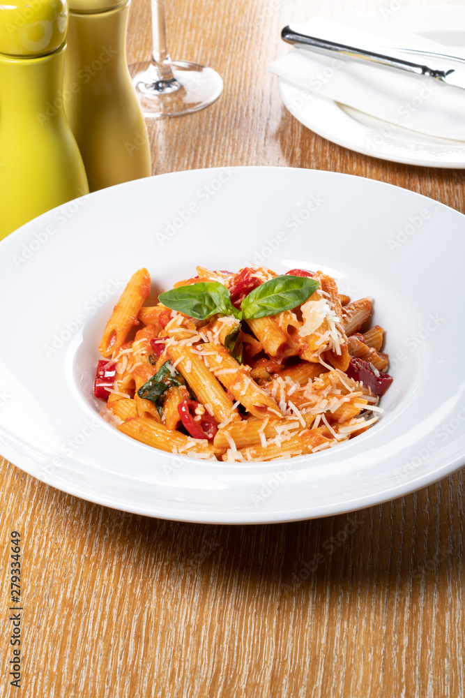 Pasta penne Napoli, traditional italian cuisine dish, chili, tomato and parmesan sauce, in a white or black plate, restaurant setting Pasta penne Napoli, traditional italian cuisine dish, chili, tomato and parmesan sauce, in a white or black plate, restaurant setting