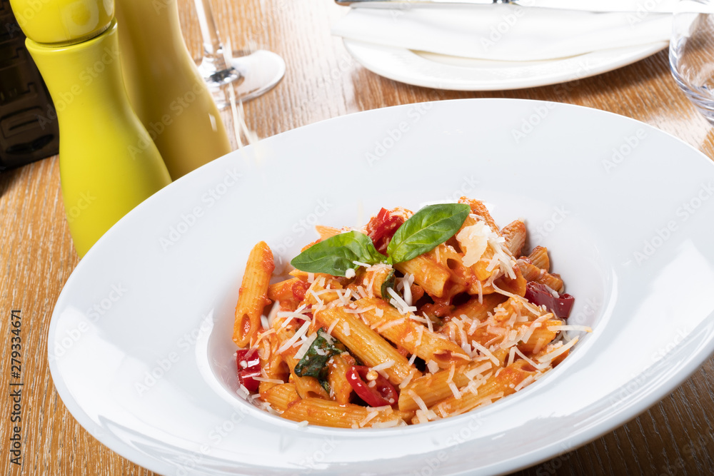 Pasta penne Napoli, traditional italian cuisine dish, chili, tomato and parmesan sauce, in a white or black plate, restaurant setting