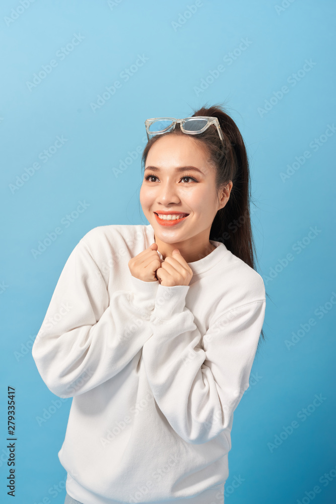 Happy woman keeps hands under chin looks joyfully at camera, notices something very pleasant, isolated over light blue background Happy woman keeps hands under chin looks joyfully at camera, notices something very pleasant, isolated over light blue background