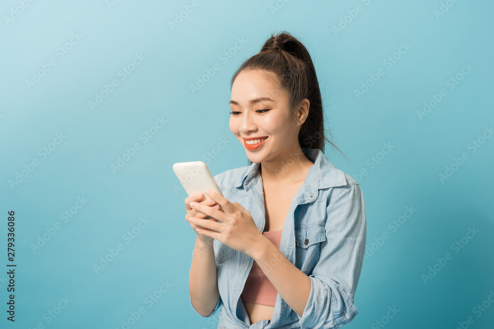 Asian woman 20s holding mobile phone and smiling over blue background Asian woman 20s holding mobile phone and smiling over blue background