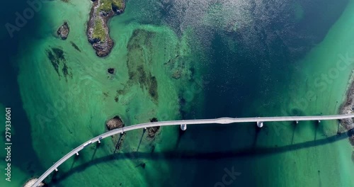 Aerial top-down pan shot of beautiful road bridge in amazing fjord scenery with green and blue water shades.