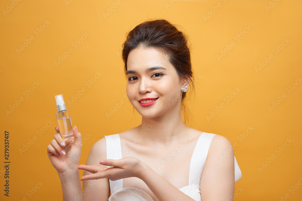 Beautiful asian woman standing , holding spray bottle, Yellow background Beautiful asian woman standing , holding spray bottle, Yellow background