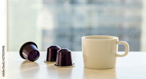 Espresso coffee cup and coffee capsules on a white table. Blur window background