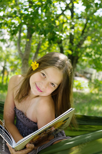 Beautiful girl reading a book and lying on a hammock in the garden