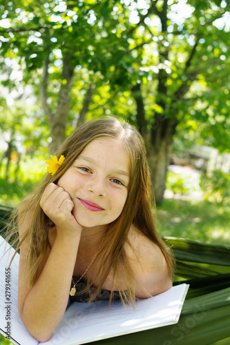 Beautiful girl reading a book and lying on a hammock in the garden