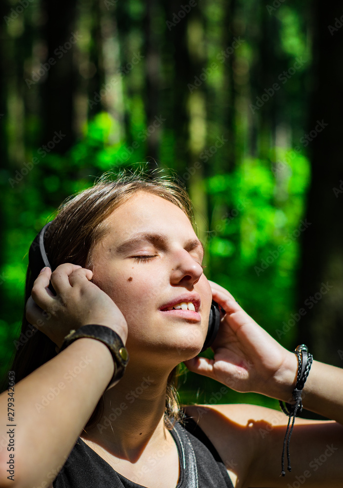 Outdoor portrait of young teenager brunette girl with long hair. Happy young woman listening to music with headphones in forest.