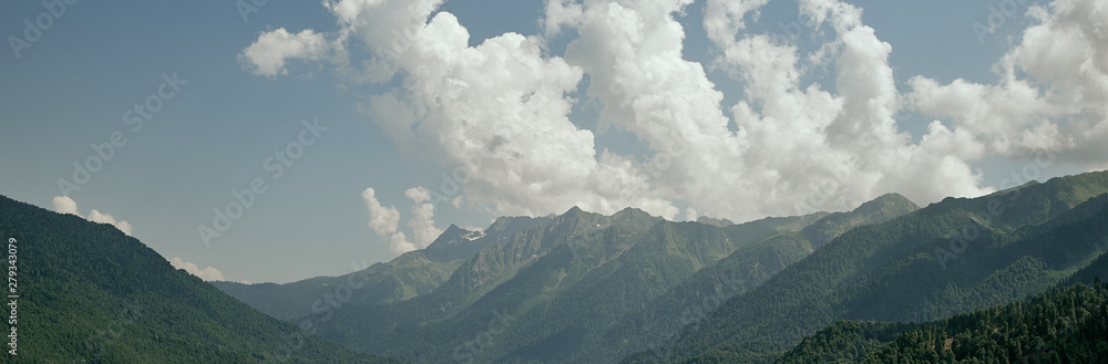 View of the green mountains illuminated by bright sunlight on the background of great white clouds.