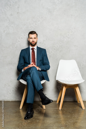 handsome bearded man sitting with crossed legs on chair in office