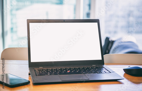 Blank screen laptop on a wooden desk, blur winddow background