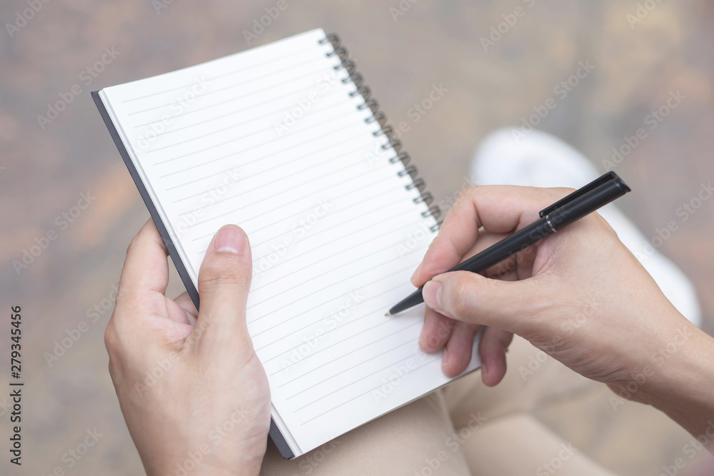 close up hand young man are using pen writing Record Lecture note pad into  the book sitting on the chair outdoor. Blank book page copy write a  message. Stock Photo | Adobe