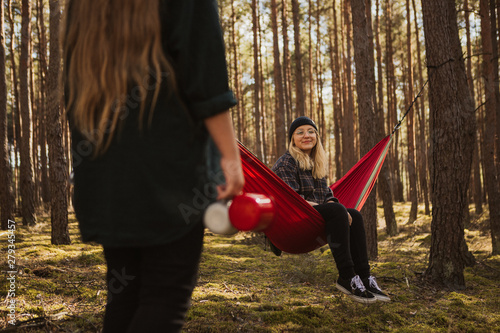 Happy young hipster girl enjoys life and nature on hammock with other woman in the summer forest. © Lukasz