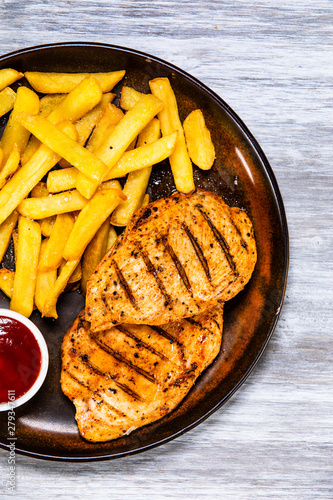 Grilled chicken fillets with french fries on wooden table