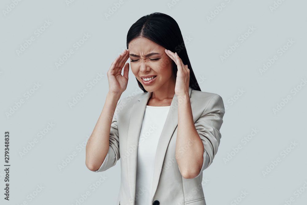 Feeling the pain. Frustrated young Asian woman making a face while standing against grey background Feeling the pain. Frustrated young Asian woman making a face while standing against grey background