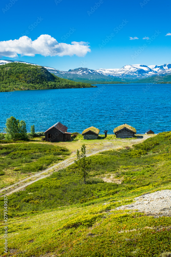 Typical mountain huts by the lake in summer, on snowy mountain horizon, southern Norway