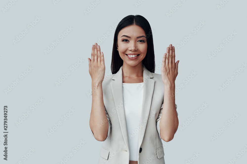 Feeling playful. Attractive young Asian woman looking at camera and smiling while standing against grey background Feeling playful. Attractive young Asian woman looking at camera and smiling while standing against grey background