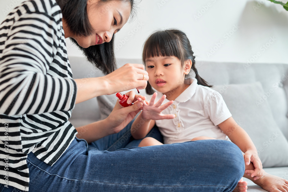 Beautiful young mother is painting the nail varnish to her cute little daughter Beautiful young mother is painting the nail varnish to her cute little daughter