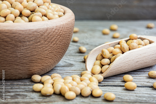 Dried raw soya in wooden bowl and measuring cup on wooden background. Soybeans in a bowl with ladle. Natural decoration with soy.