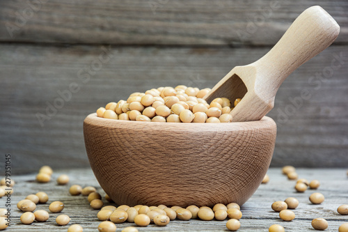 Dried raw soya in wooden bowl and measuring cup on wooden background. Soybeans in a bowl with ladle. Natural decoration with soy.
