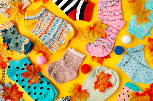 Socks for autumn on a yellow background. Colorful socks and maple leaves on a yellow background. Clothes for the autumn season. Socks for adults and children.