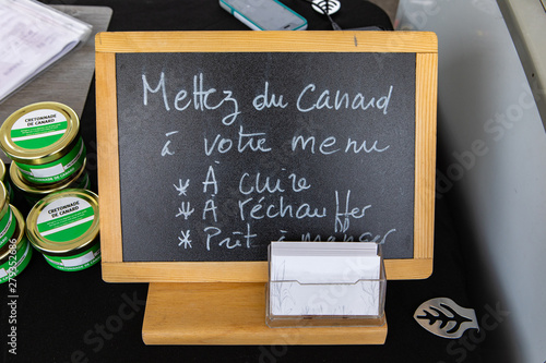 Organic produce sold at farmer's market. A small French chalkboard is seen up close, saying put some duck in your menu, to cook, warm up, ready to eat, next to tins of duck cretonnade for sale. photo