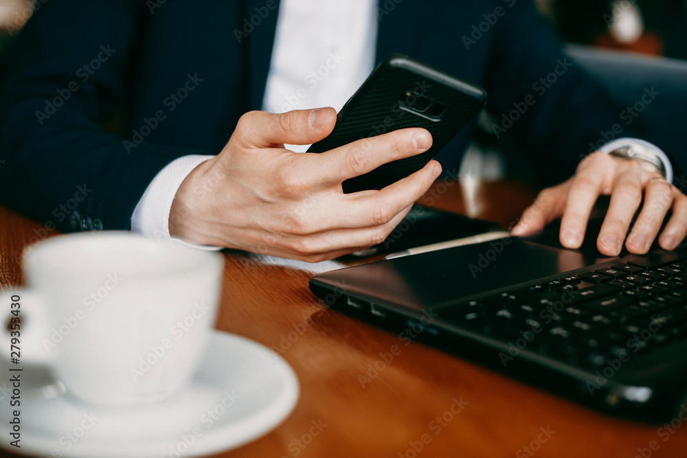 Male hand dressed in suit holding a smartphone and while sitting at a table indoor. Male hand dressed in suit holding a smartphone and while sitting at a table indoor.