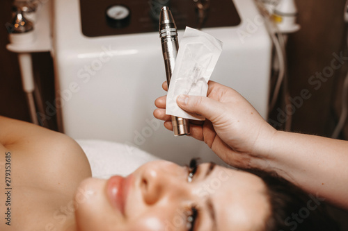 Cosmetologist hand holding a rf radiofrequency equipment near a female face .