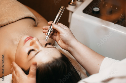 Φωτογραφία Close up of a lovely female doing radiofrequency procedures on her face by a cosmetologist in a wellness center