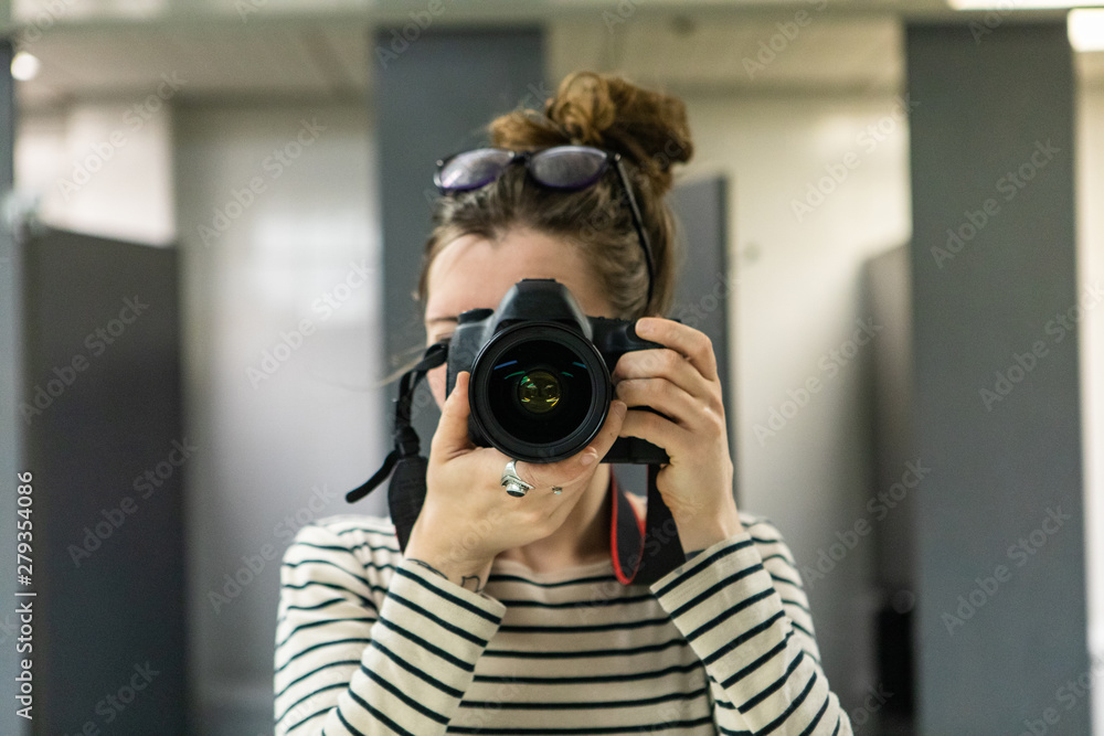 Atmosphere during corporate conference. A close up and front view of a young Caucasian woman taking a photograph behind a professional camera. Looking straight into the lens with room for copy. Atmosphere during corporate conference. A close up and front view of a young Caucasian woman taking a photograph behind a professional camera. Looking straight into the lens with room for copy.
