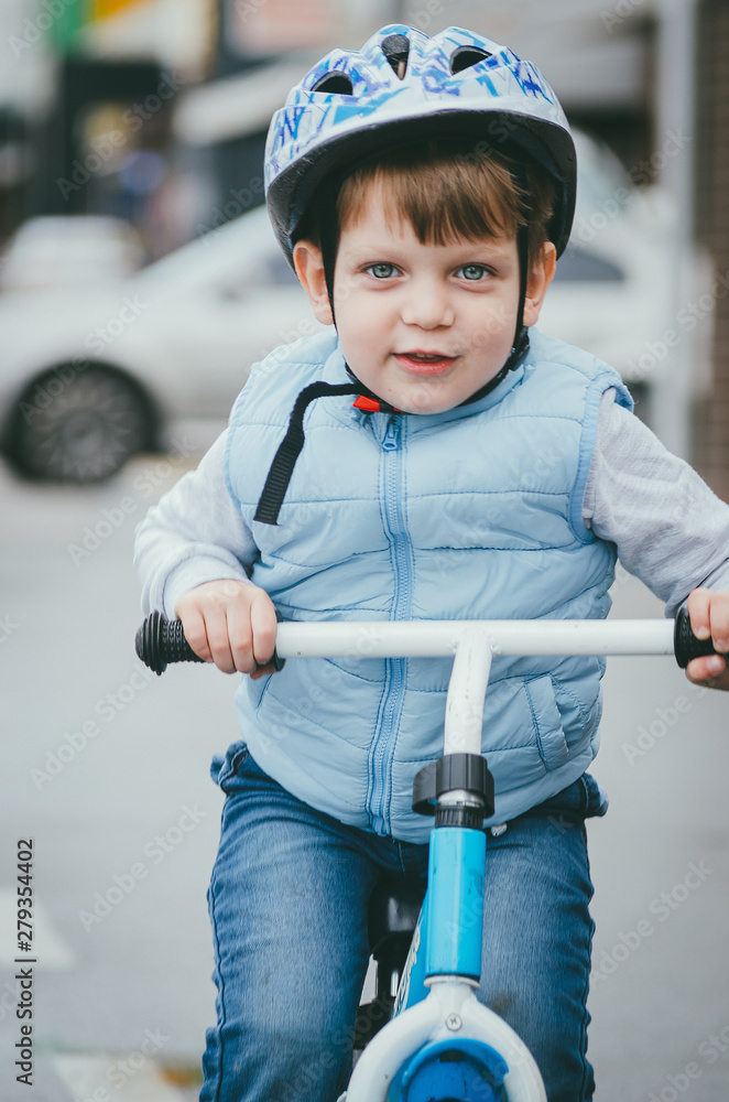 cute boy of three years old in a blue vest and protective helmet rides a bike run along a city street. Children's useful games in the fresh air. Fun sport