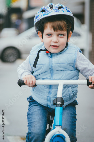 cute boy of three years old in a blue vest and protective helmet rides a bike run along a city street. Children's useful games in the fresh air. Fun sport