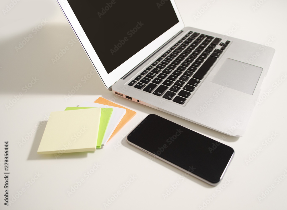 Laptop and phone on a table with infinite white background with note pots. Laptop and phone on a table with infinite white background with note pots.