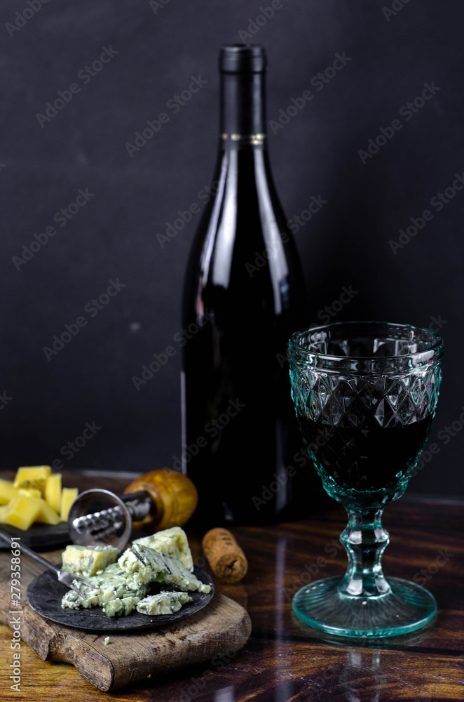 Vintage wine glasses and bottle of red wine on a wooden table. Blue cheese cut on the old cutting board