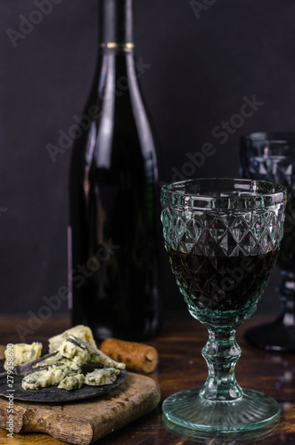 Vintage wine glasses and bottle of red wine on a wooden table. Blue cheese cut on the old cutting board