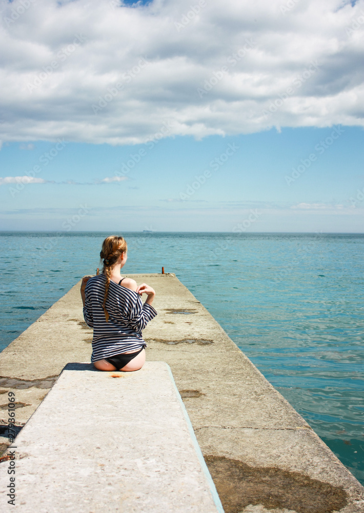 A blonde girl in a black bikini swimsuit and marine vest is preparing for swimming in the sea in the summer on vacation