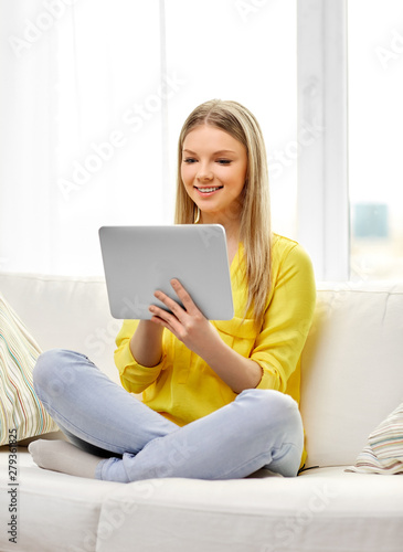people, technology and leisure concept - happy young woman or teenage girl sitting on sofa with tablet pc computer at home